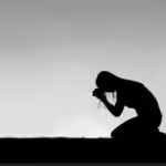 Silhouette of a woman kneeling in prayer against a bright sky