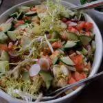 Delicious and healthy organic vegetable salad with radishes, cucumbers, and frisée in a white bowl.