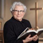 Elderly woman in a church holding an open Bible, smiling.