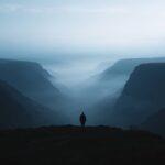Silhouette of a lone person standing on a cliff overlooking a misty canyon.